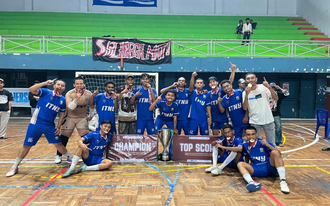 Group of young male athletes in blue uniforms celebrate indoors, posing with a trophy and wearing medals. A banner reads CHAMPION and another reads TOP SCORE in front of the team.